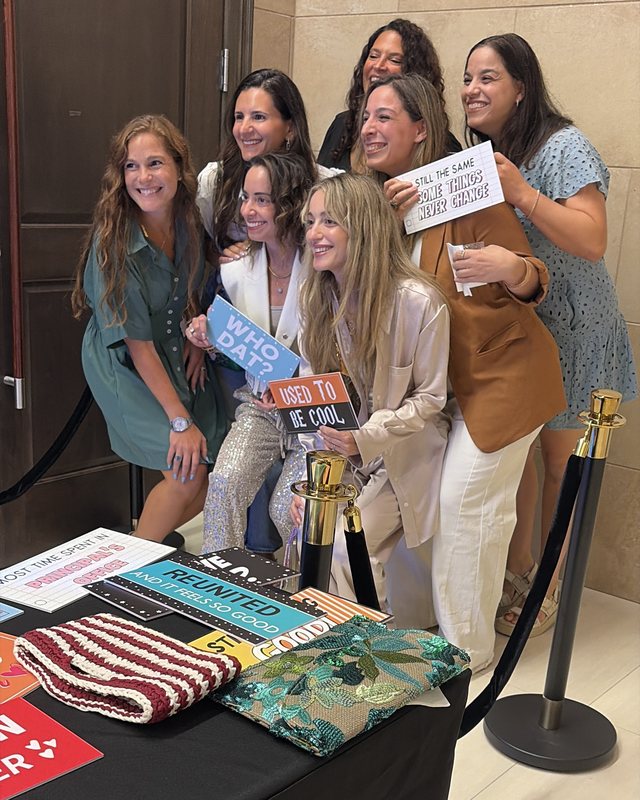 A group of smiling guests holding playful reunion signs together at a Mabooth mirror photo booth event